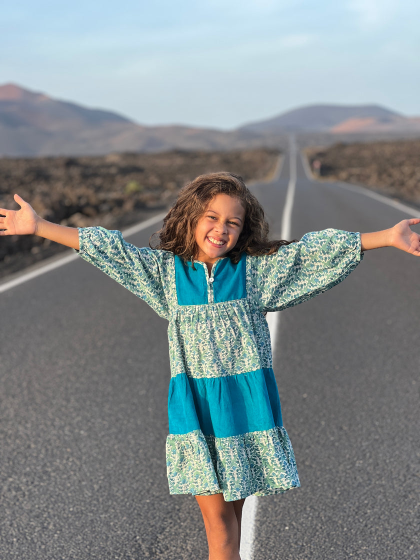 Knee length tiered dress with alternate tiers in plain turquoise fabric and green floral fabric. With button fastenings on the placket.