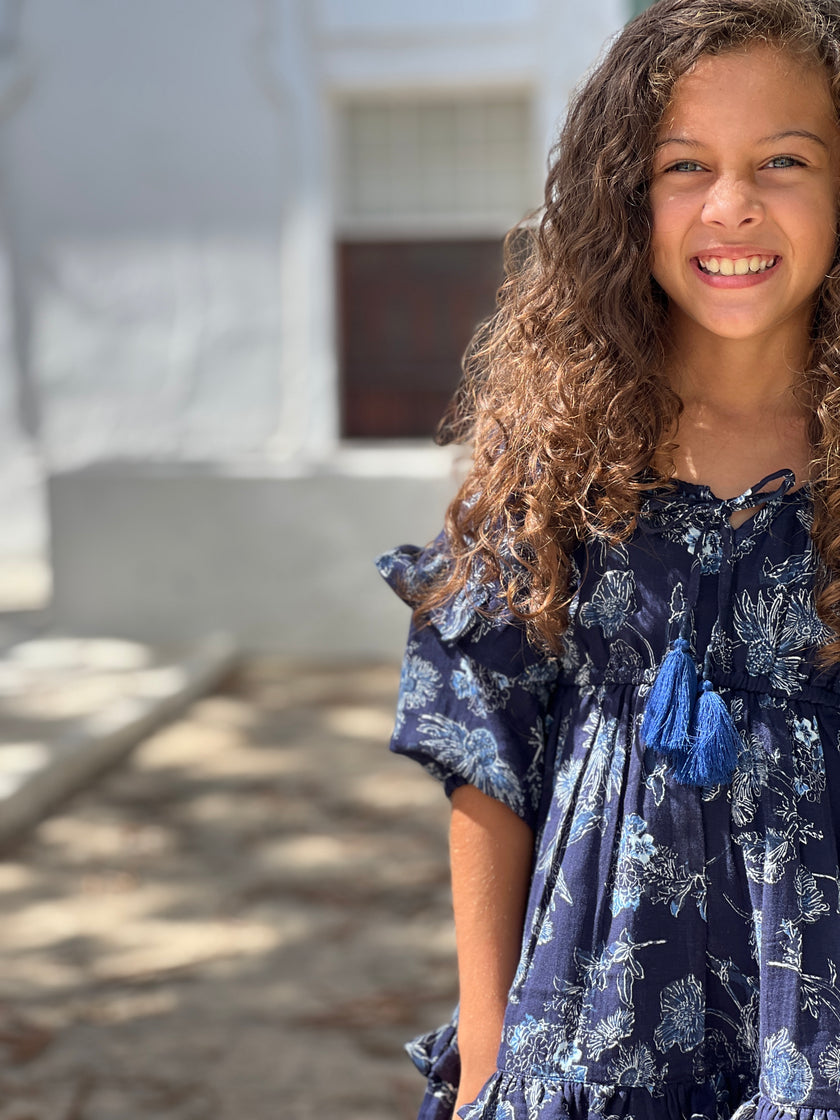 Sweet knee length gypsy dress with double frill at the hem and tassel ties at the neck and waist. In our dark blue and white floral print and with long sleeves.